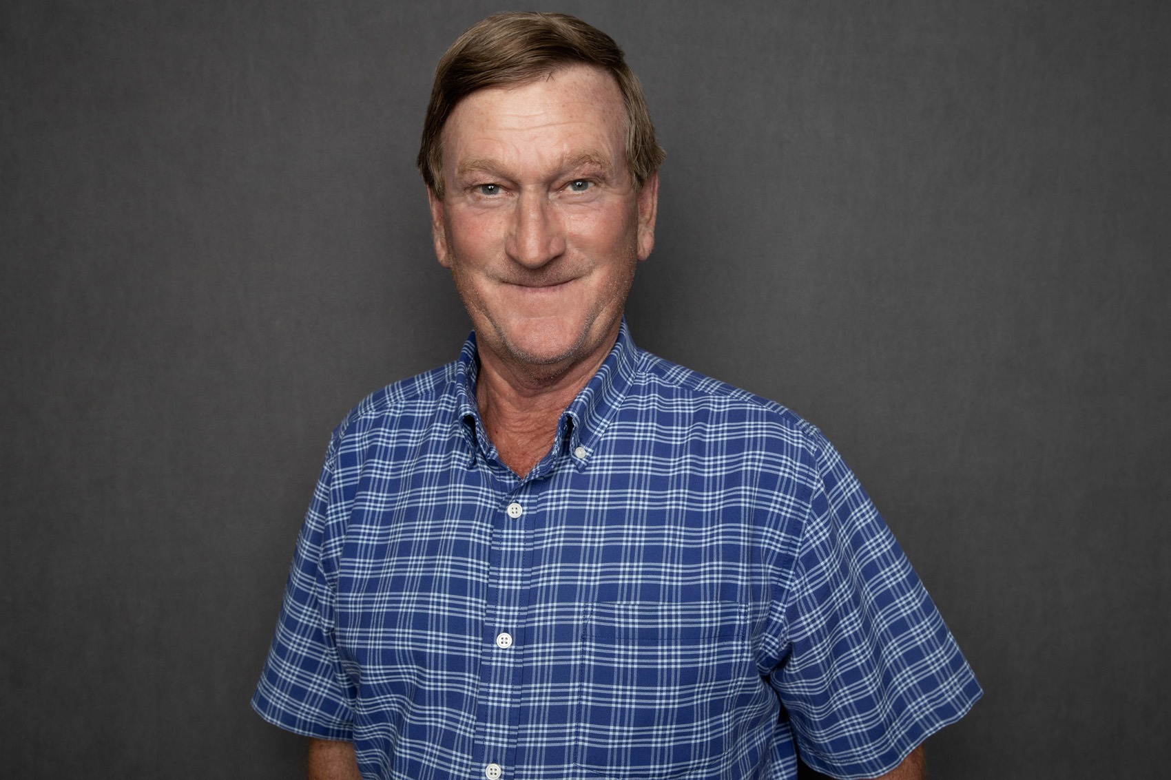 Portrait of JR Howell, a senior superintendent at Crain Construction, in professional attire, smiling and standing against a plain grey background.